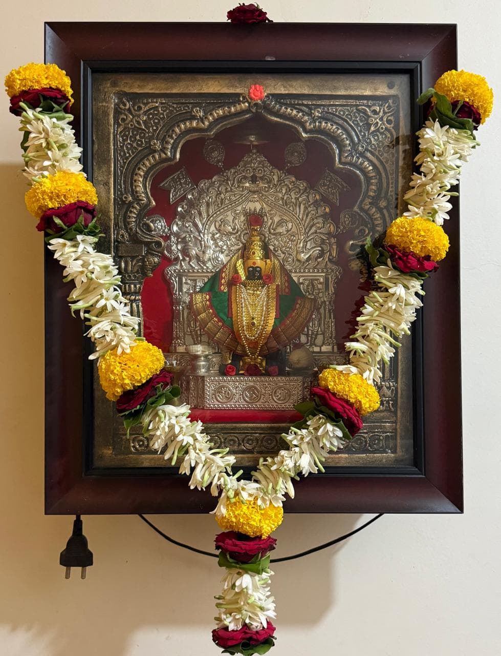Devi frame draped with a marigold, rose and jasmine garland for daily darshan