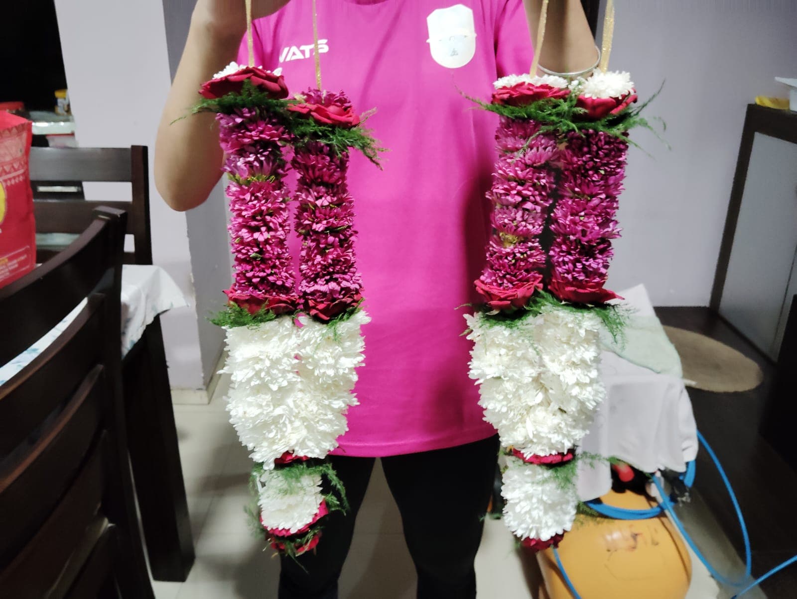 A pair of handmade rose and sevanti garlands held up fresh from the workshop